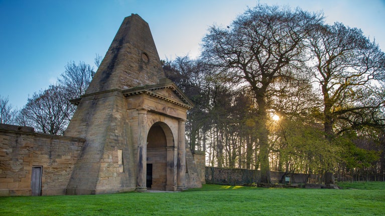 The Obelisk Lodge captured in the spring with new leaves appearing on the trees in the background and the sun coming up behind the trees